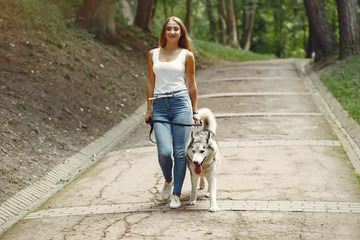Naklejka na ściany i meble Beautiful girl in a white t-shirt. Woman in a summer park. Lady with a dog