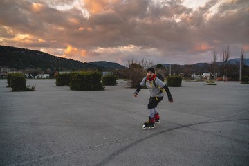 Man skating with inline skates with a backpack, hat and scarf in an urban parking
