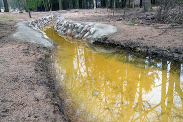 A ditch full of runoff water flowing along the road lined with stone in the countryside