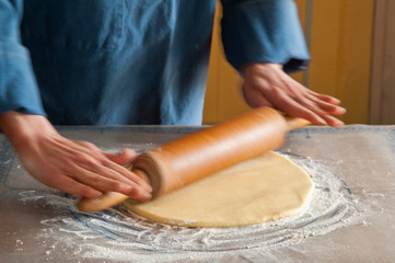 Personne utilisant un rouleau en bois pour préparer une pate à tarte.  Person using a wooden...