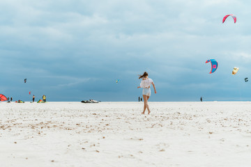 Obraz premium view from afar of a beach with flying kites and a girl running away