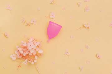 Menstrual cup with hydrangea flowers on pastel orange background.
