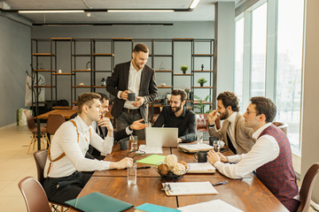 caucasian business people in formal wear sit coworking at work place, have free time, drinking tea or cup of coffee in modern boardroom