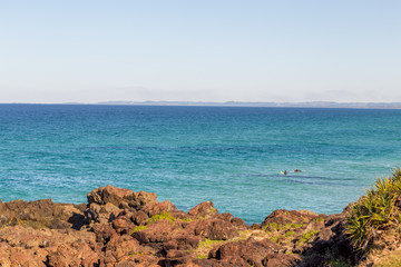Sunny morning, two surfers waiting for waves with jagged rocks in the foreground. Copy space