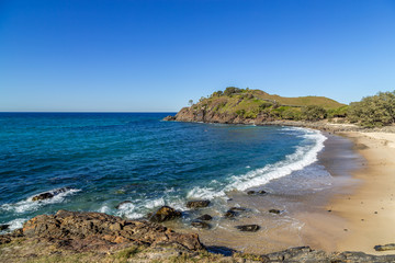 Deserted beach with small waves breaking on the shoreline and green hill filled with trees