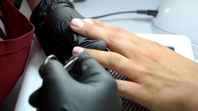 Manicure master in black gloves cuts a cuticle from a client finger with thin nail scissors