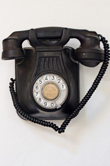 Old black telephone hanging on a white wall
