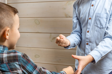 A 4-year-old boy in a blue klepy shirt cries on a light wooden background and his brother, 10 years old, is standing.