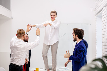 Obraz premium young happy caucasian team celebrate victory in modern office, after successful win or completion of project, togetherness of business team