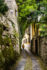 Fototapeta na wymiar Stone path between ancient buildings and moss-covered walls on Isola San Giulio, Italy