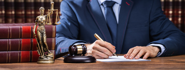 Lawyer Signing Documents Near Mallet And Scales