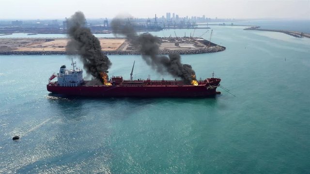 Aerial image over Oil Tanker Ship Burning Under attack Close to Harbor Aerial view with visual effect elements simulates realistic vision of Oil Tanker on fire with smoke  and Helicopter Close to Harb