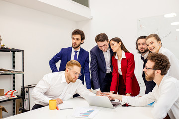 young caucasian good-looking people in formal wear stand next to their female boss or manager in red blazer, offer to implement new business project, look at laptop and consider