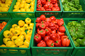 Red, yellow and green peppers in a plastic box on a store counter. Sweet pepper in a basket. Vegetable department in a supermarket.