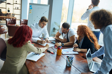 Successful young team of caucasian coworkers making great creative business discussion in modern coworking office, panoramic windows background