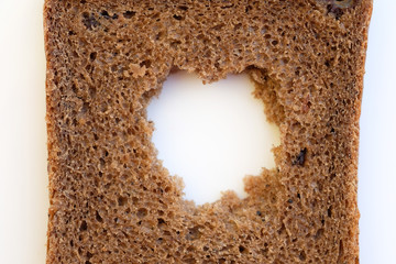 A slice of black bread with a hole in the middle. Rye flour bread on a white background top view.