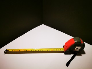 A tape measure for rolling in and out with fixed function in a red black case and a yellow measuring bar with black numbers on a white background