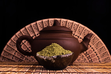 matcha, green tea in clay pot and a kettle on wooden background with a fan. food photography