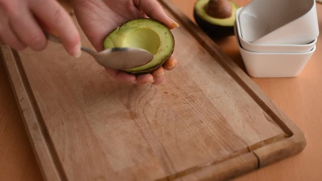 Verarbeiten einer Avocado. Frauenhand beim Auslöffeln einer Hälfte von einer Avocado