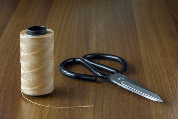 spool of beige thread and black scissors on a yellow wooden table surface