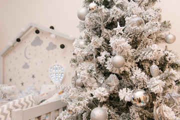 Wooden grey white children's bed in the shape of a house with stars and moon, a balloon on the wall next to a Christmas tree, selective focus