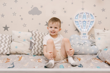 Little cute baby boy sitting in the children room in a wooden bed house with night lights in the shape of a balloon