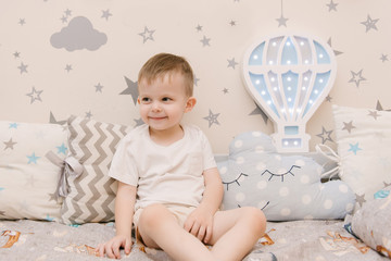 Naklejka premium Little cute baby boy sitting in the children room in a wooden bed house with night lights in the shape of a balloon