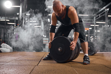 Bright modest powerlifter spending evening in gym, preparing barbell for training, fixing weight...