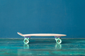 Plastic skateboard on the green wooden floor against blue wall. Side view © Dmitry Zimin