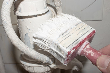 Painting the sink siphon with white paint with a brush.Painting plumbing fixtures with white paint.