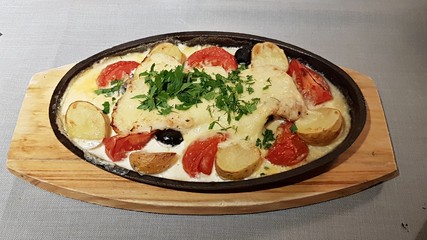 Baked meat with potatoes and tomatoes in a pan and served on a wooden board
