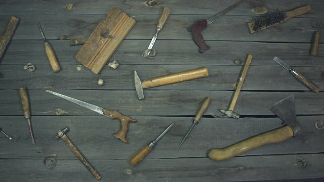 Basic wood processing tools. Slow motion. Top view.  Wooden sawdust is falling on top of the table.  On the table are mixed work tools (screwdrivers, chisels, hammers, ax, awl, metal brush, jointer).