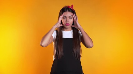 Young beautiful woman with long hair having headache, studio portrait. Girl putting hands on head, isolated on yellow background. Concept of problems and headache.