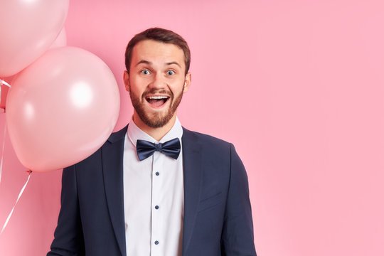 Good-looking man with beard wearing suir stand holding pink air balloons and happily smile, isolated pink background. Celebrating concept