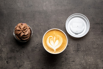 Chocolate cupcake and cappuccino in paper cup on gray background top view