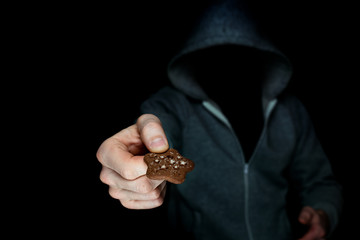an unknown man in a hood holds out a cookie in his hand, trying to treat