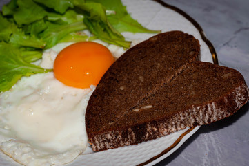 selective focus of tasty traditional breakfast with fried egg protein and whole yolk, slices of heard-shaped bread and greenery on white plate