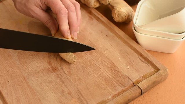 Frauenhand schneidet Scheiben von einer Ingwerwurzel ab