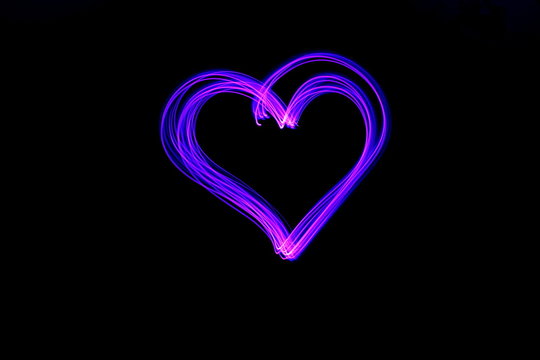 Long exposure light painting, vibrant pink and purple outline of a heart shape, against a clean black background.  Light painting photography.