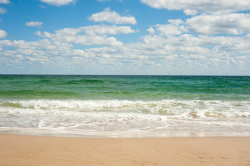 Blue sea wave on sandy beach. Beautiful sea waves on a background of blue sky with clouds on a sunny summer day. Sea waves roll on yellow sand.