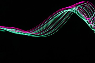 Long exposure light painting, vibrant pink and green color in abstract swirl against a clean black background.  Light painting photography.