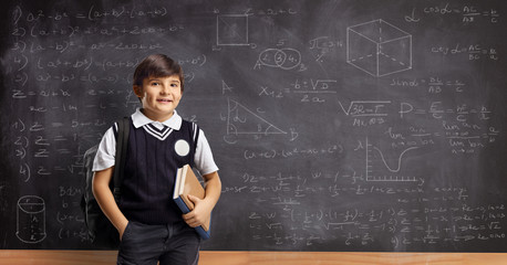 Schoolboy with books and backpack standing in front of a school blackboard with math formulas