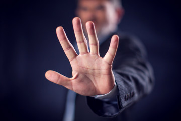Businessman in suit showing stop gesture with hands in front of black background