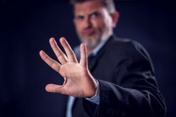 Businessman in suit showing stop gesture with hands in front of black background