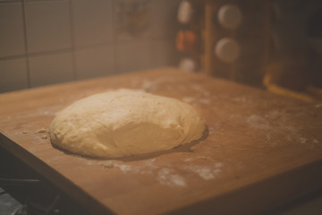 Closeup of pizza dough with flour on a wooden cutting board in the kitchen