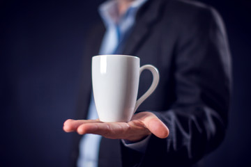 Businessman in suit holding cup of tea or coffee in hand in front of black background