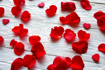 Red rose petals and small red wooden hearts on a white wooden background. St. Valentine's Day background. 