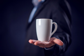 Businessman in suit holding cup of tea or coffee in hand in front of black background