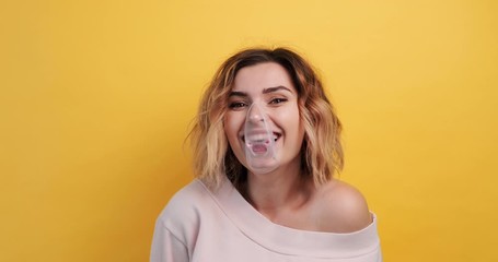 Portrait young sexy girl diligently inflates a bubble of chewing gum and rounds her eyes from the effort, bursts it laughing on an isolated yellow background. Pleasure. The emotions of people