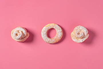 Row of two homemade baked buns in form of rose and donut powdered of sugar on pink background. Top view. Close-up